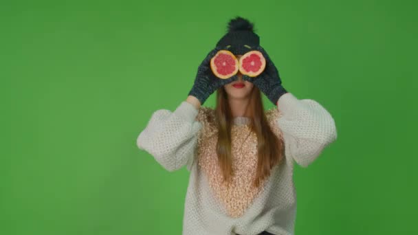 Nettes Mädchen mit offenen blauen Augen in einem weißen Pullover hält zwei Grapefruits. — Stockvideo