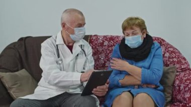 Yaşlı bir doktor tablette hangi ilacı alması gerektiğini gösteriyor.. 