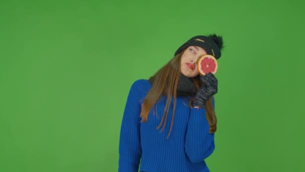 Ein junges Mädchen in blauem Pullover und Hut, das eine Grapefruit in der linken Hand hält, ist aufgebracht. — Stockvideo