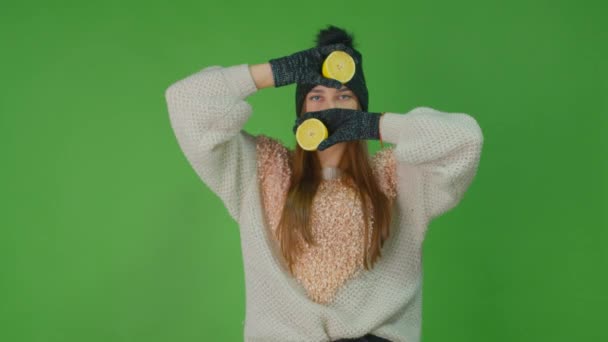 Πορτρέτο ενός χαμογέλασε νεαρό κορίτσι κρατώντας φέτες λεμονιού φρούτων και κοιτάζοντας κάμερα πάνω από το πράσινο φόντο τοίχο. — Αρχείο Βίντεο