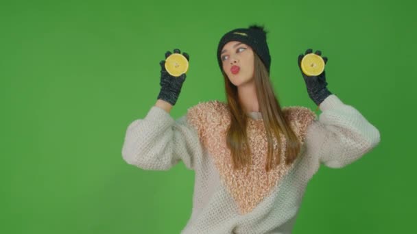 Молодая женщина в черных перчатках держит два ломтика лимона, стоящих на зеленом фоне. — стоковое видео