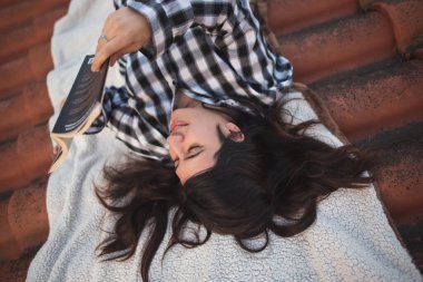 Evinin çatısında rahatlama anında kitap okuyan bir kadın.