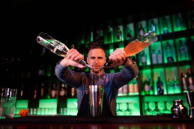 Bir barda kokteyl hazırlarken barmenlik yapan genç bir adam.