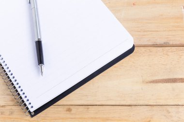 Ahşap masasında kalem olan boş beyaz bir defter. Yüzeyin derinliği