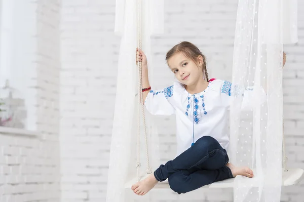 Молодая девушка в вышивке на качелях — стоковое фото
