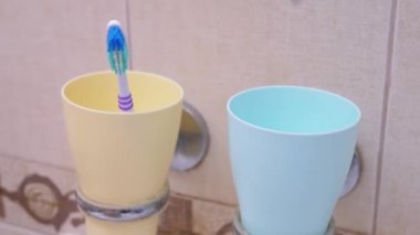 Banyodaki Mavi Plastik Kupaya kirli bir diş fırçası at. Yakın plan. 4k