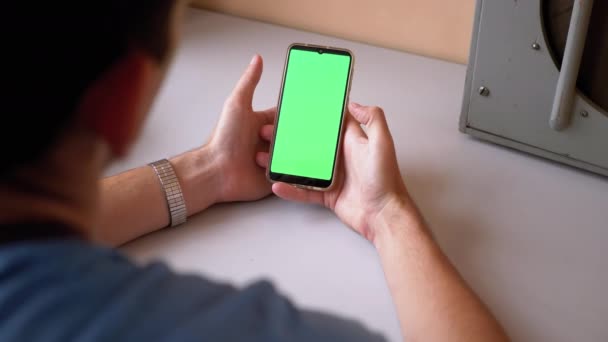 Hombre sostiene un teléfono inteligente con una pantalla táctil verde en la mesa. Mirando pantalla — Vídeo de stock