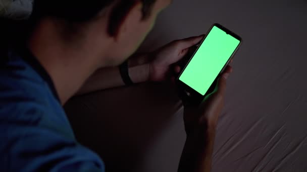 Homme dans l'obscurité sur lit tient et examine Smartphone avec écran tactile vert. — Video