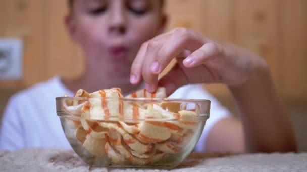 Hungriga tonåringar sätter flis från en tallrik i munnen hemma. Boy äter snabbmat — Stockvideo