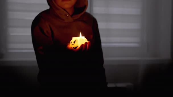Silueta chlapce v Hoodovi. Ruka drží hořící dýňovou svíčku v temném pokoji — Stock video