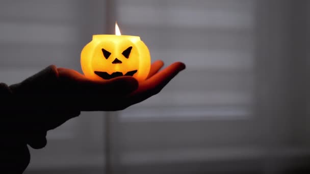 Kid Hand egy égő sütőtök gyertyát tart egy sötét szobában. Éjszaka Halloween. — Stock videók