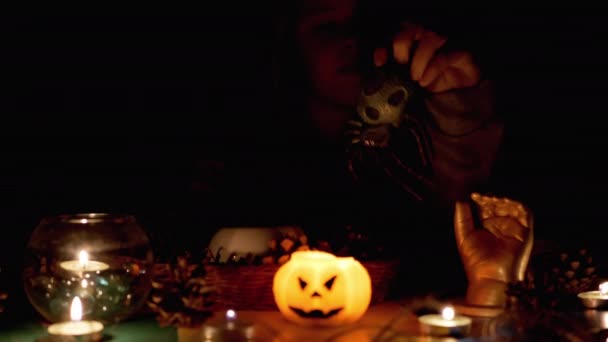 Seltsamer Junge mit Kapuze spielt an Halloween mit Spinne bei Kerze im dunklen Raum — Stockvideo