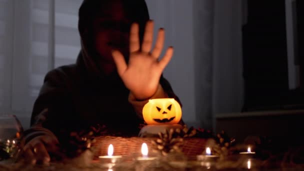 Kluk v kápi vykouzlí dýňovou svíčku v tmavém halloweenském pokoji — Stock video