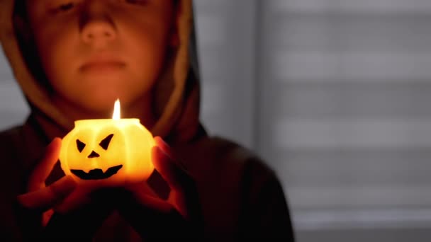Silueta chlapce v Hoodovi. Ruka drží hořící dýňovou svíčku v temném pokoji — Stock video