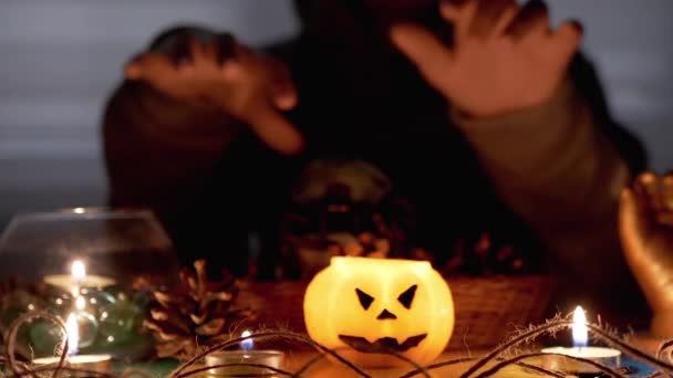 Kluk v kápi vykouzlí dýňovou svíčku v tmavém halloweenském pokoji — Stock video
