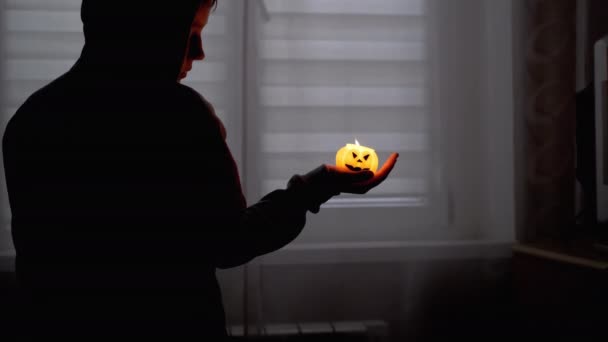 Silhouet van Boy in Hood. Hand houdt een brandende pompoenkaars in een donkere kamer — Stockvideo