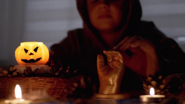 Ragazzo sciamano incappucciato evoca sopra la candela di zucca nella stanza oscura di Halloween — Video Stock