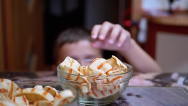 Hungriger Teenager stiehlt Kartoffelchips vom Tisch in einem Teller, während niemand hinsieht — Stockvideo
