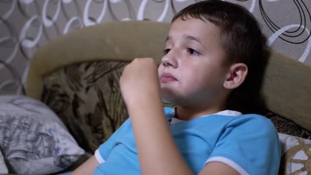 Улыбающийся голодный ребенок смотрит телевизор, ест крекеры из стаи. Пассивный отдых — стоковое видео