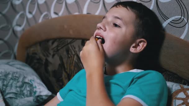 Sonriente niño hambriento viendo la televisión, comiendo galletas fuera de paquete. Descanso pasivo — Vídeos de Stock