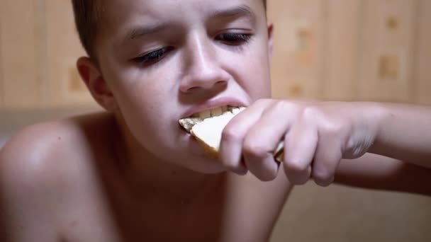 Un niño hambriento muerde un pedazo de pan y se lo come. Comida rápida en casa en la cocina — Vídeos de Stock