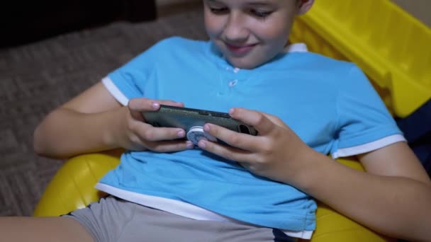 笑顔の男の子はリラックスした状態で自宅でスマートフォンでモバイルゲームをプレイ — ストック動画