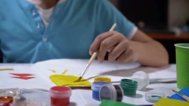 Niño con un pincel en la mano pinta el sol con pintura amarilla en la hoja blanca de papel — Vídeos de Stock