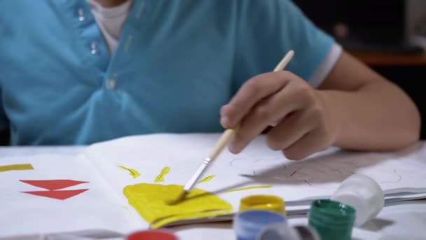 Niño con un pincel en la mano pinta el sol con pintura amarilla en la hoja blanca de papel — Vídeos de Stock