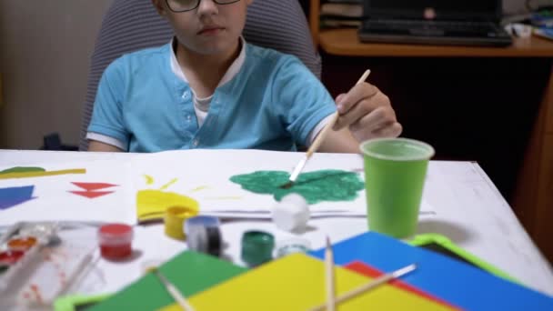 Talent Boy in bril en blauwe T-shirt tekent afbeelding met groene verf op papier — Stockvideo