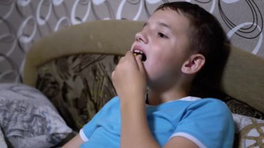 Gülümseyen Aç Çocuk TV izliyor, paketten kraker yiyor. Pasif Dinlenme