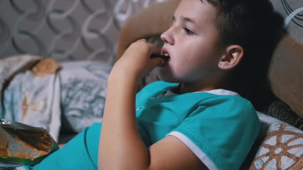 Gülümseyen Aç Çocuk TV izliyor, paketten kraker yiyor. Pasif Dinlenme — Stok video