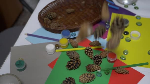 Borovicové šišky padají na stůl se školními potřebami, tužkami, barevným papírem. Art — Stock video