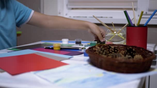 Bambino mano stende pennelli, vernici ad acquerello, forbici sul tavolo. Artista ragazzo — Video Stock