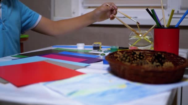 Bambino mano stende pennelli, vernici ad acquerello, matita sul tavolo. Artista ragazzo — Video Stock