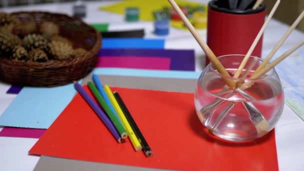 Auf dem Tisch liegen zufällig angeordnete Avocarelfarben, Bleistifte, Pinsel, buntes Papier — Stockvideo