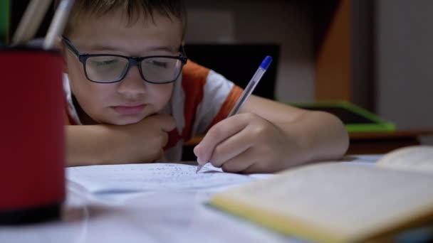 Schoolboy γράφει με το αριστερό χέρι στο σημειωματάριο, χρησιμοποιώντας λαβή. Online εκπαίδευση στο σπίτι — Αρχείο Βίντεο