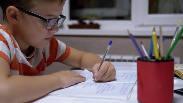 Schoolboy escreve com a mão esquerda no caderno, usando alça. Treinamento doméstico online — Vídeo de Stock