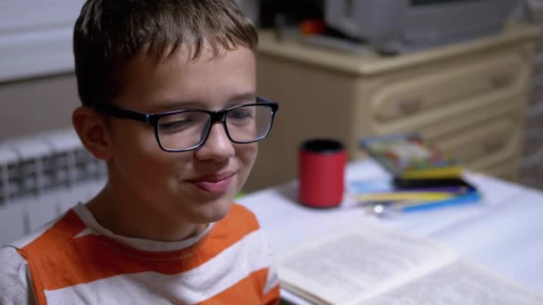 Rapaz inteligente com óculos Sorri e fala sobre livro que ele leu em casa. Leitura. — Vídeo de Stock