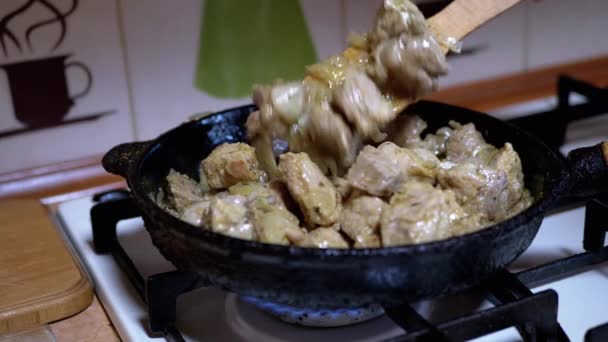 La main féminine vérifie l'état de préparation de la viande frite avec une spatule en bois. Accueil Cuisine — Video