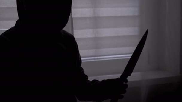 Силует самотньої дитини в капюшоні з ножем в руці біля вікна. Підліток - убивця — стокове відео