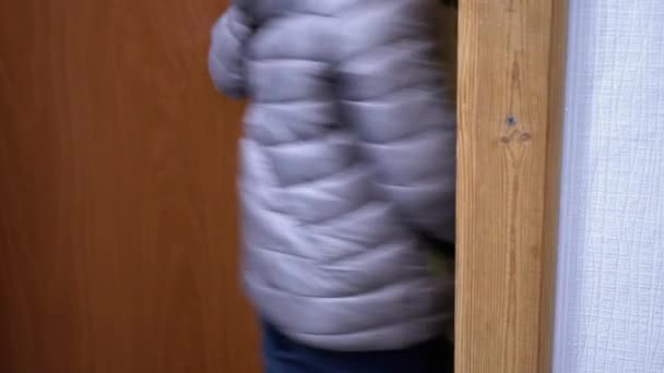 Niño con chaqueta gris abre la puerta y camina fuera de casa, alcanzando la manija de la puerta — Vídeo de stock