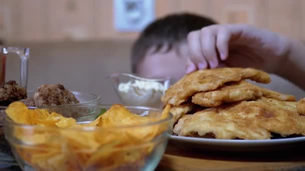 Hladový chlapec Ruka zpod stolu bere bramborové lupínky na talíři, zatímco nikdo nevidí — Stock video
