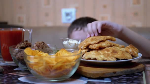 テーブルの下から空腹の少年の手は誰も見ていない間にプレートにポテトチップスを取ります — ストック動画