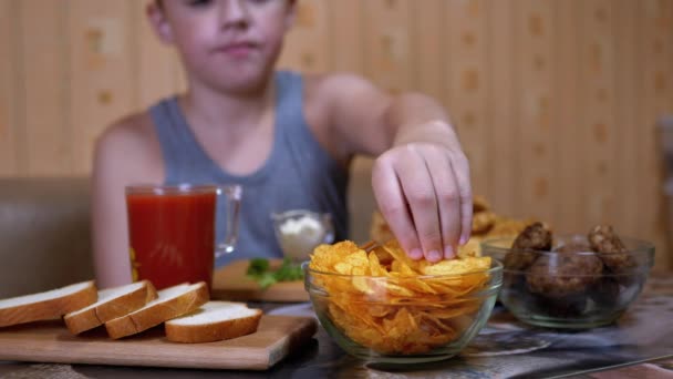 Hladová dětská ruka bere křupavé zlaté bramborové lupínky z talíře. Nevyžádané jídlo při večeři — Stock video