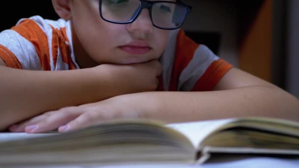 Inquisitivo, un chico serio con gafas está leyendo un libro interesante en casa — Vídeos de Stock