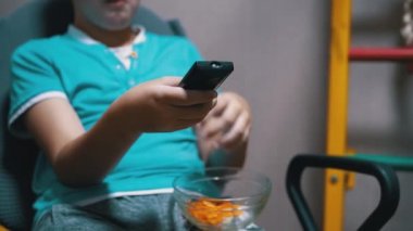 Çocuk TV karşısında oturur, patates cipsi yer, uzaktan kumanda kanalı değiştirir.