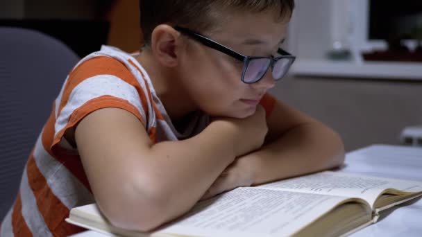 Nyfiken, en seriös pojke med glasögon är att läsa en intressant bok hemma — Stockvideo