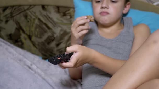 Criança com fome pressione botões com os dedos na TV remoto, Comer bolo na cama — Vídeo de Stock