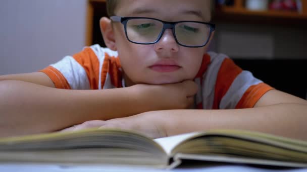 Inquisitivo, un ragazzo serio con gli occhiali sta leggendo un libro interessante a casa — Video Stock