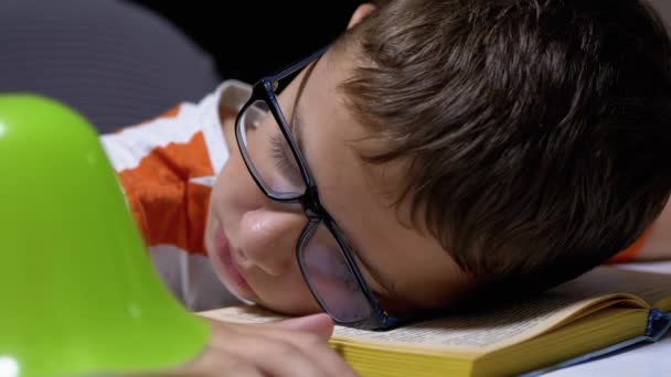 テーブルの上で読書をすると、眼鏡をかけた好奇心旺盛な少年が眠りについた。疲労、睡眠 — ストック動画